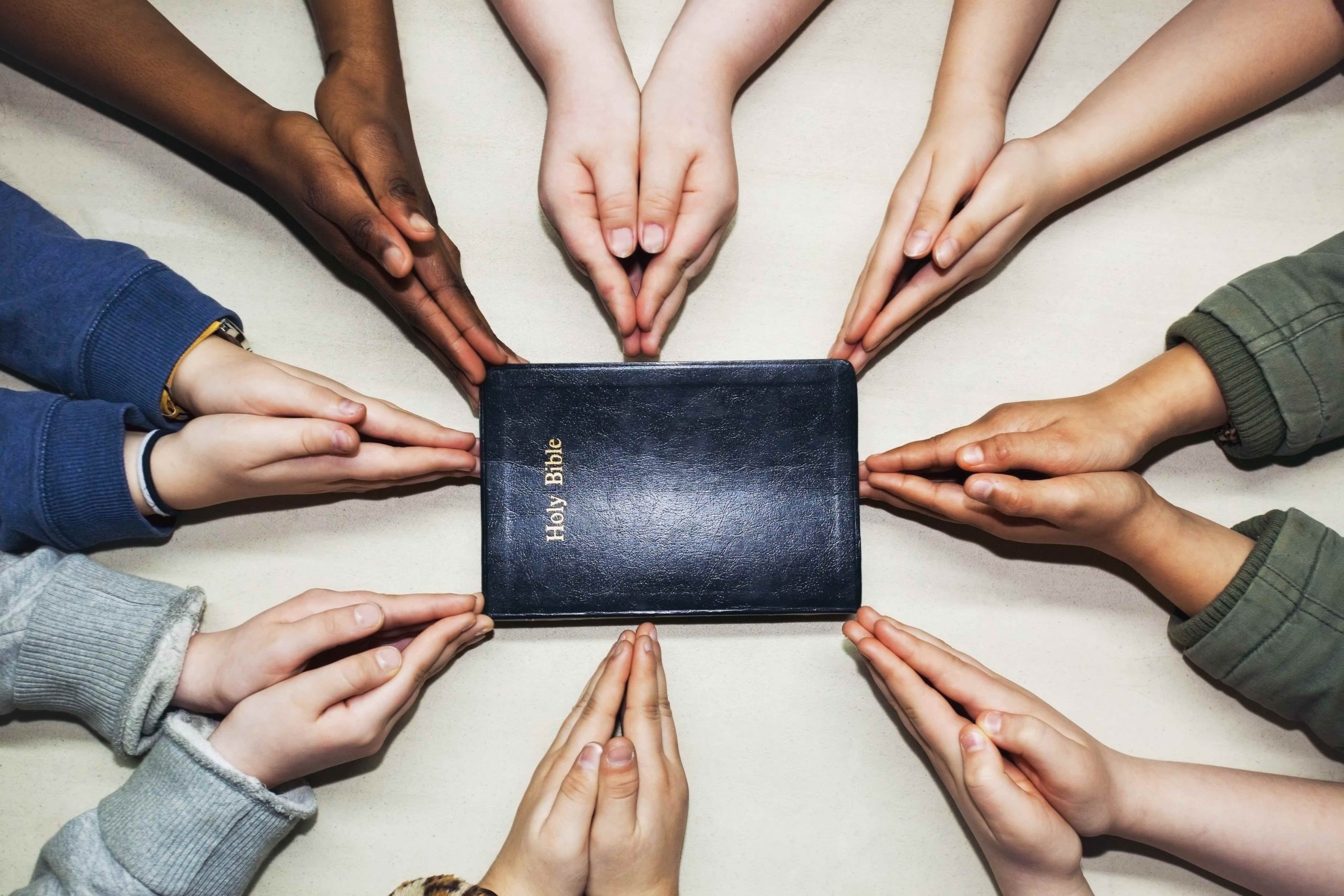 multicultural hands around Bible
